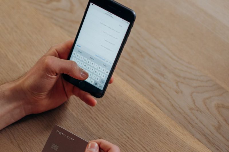 Manos con un celular y una tarjeta, comprando por internet sobre una mesa de madera